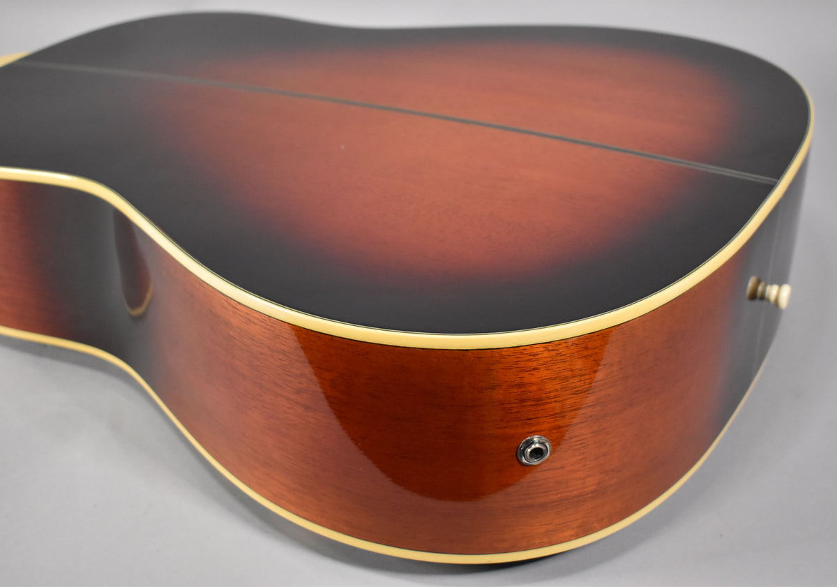 The lower bout of the sunburst acoustic guitar, showing the dark brown top fading to reddish-brown sides with cream binding and an output jack.