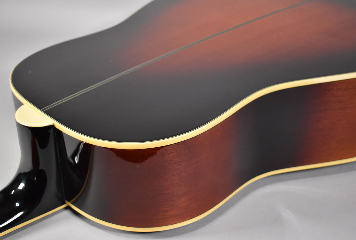 The sunburst acoustic guitar's lower bout and waist are visible, showing the dark top, brown sides, cream binding, and neck heel.