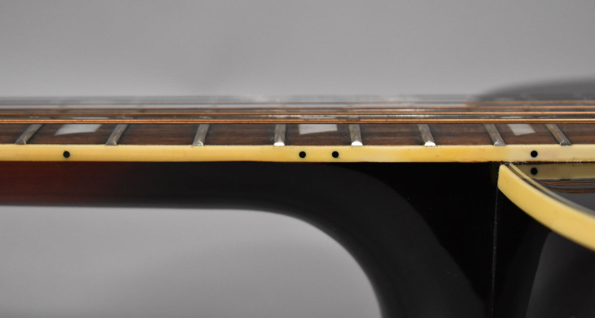 Close-up of the guitar's dark brown fretboard with rectangular inlays and cream binding, showing the neck joint and sunburst body.