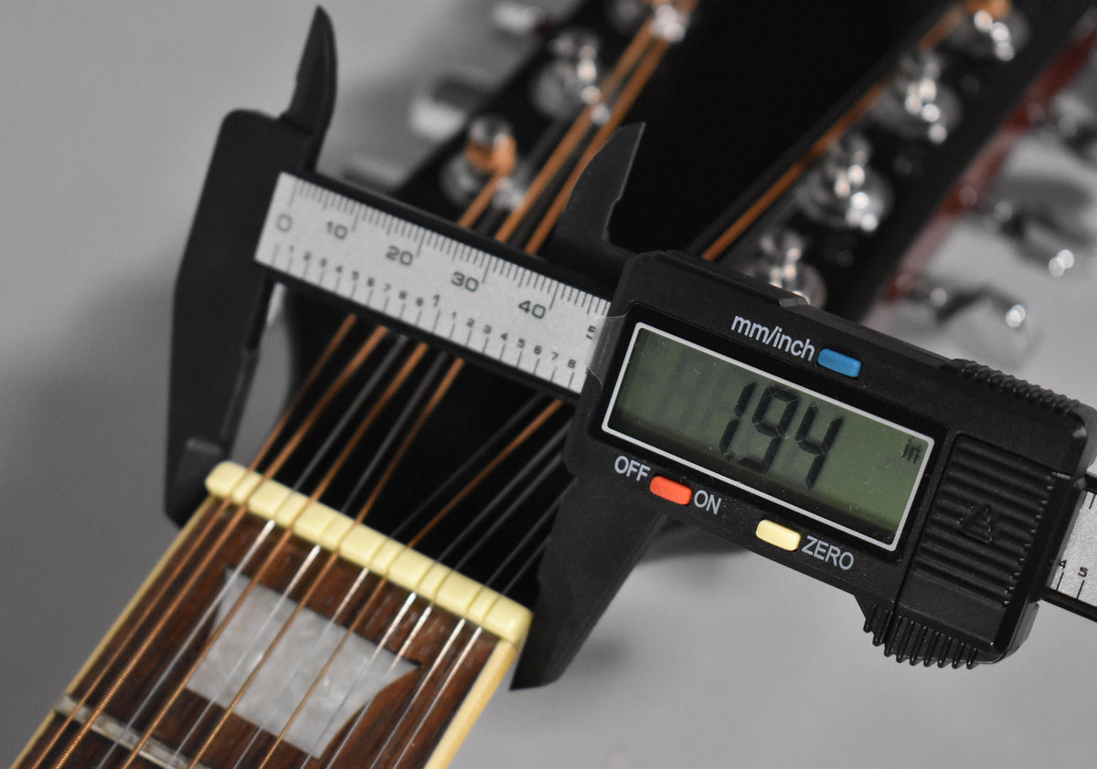 A digital caliper measures the guitar's nut width at 1.94 inches, with the fretboard and strings visible below.