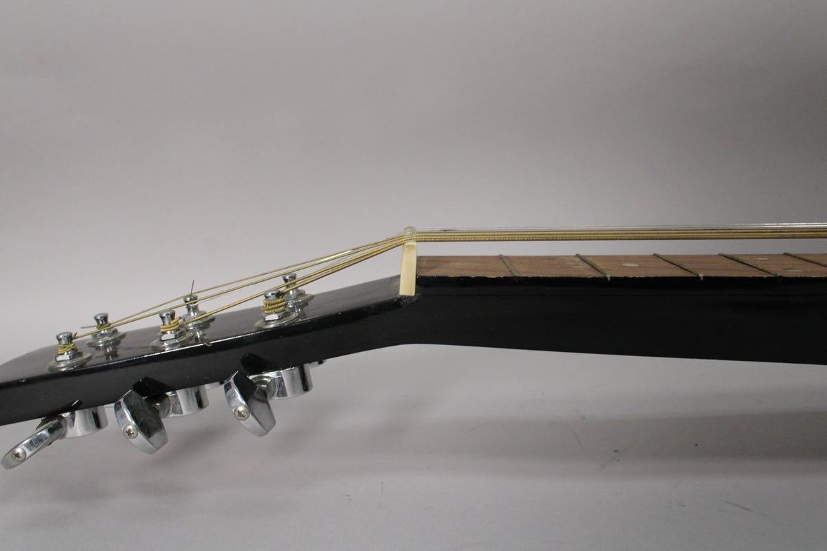 Close-up of the black headstock and upper fretboard from the side, showing six chrome tuners and a tall white nut.
