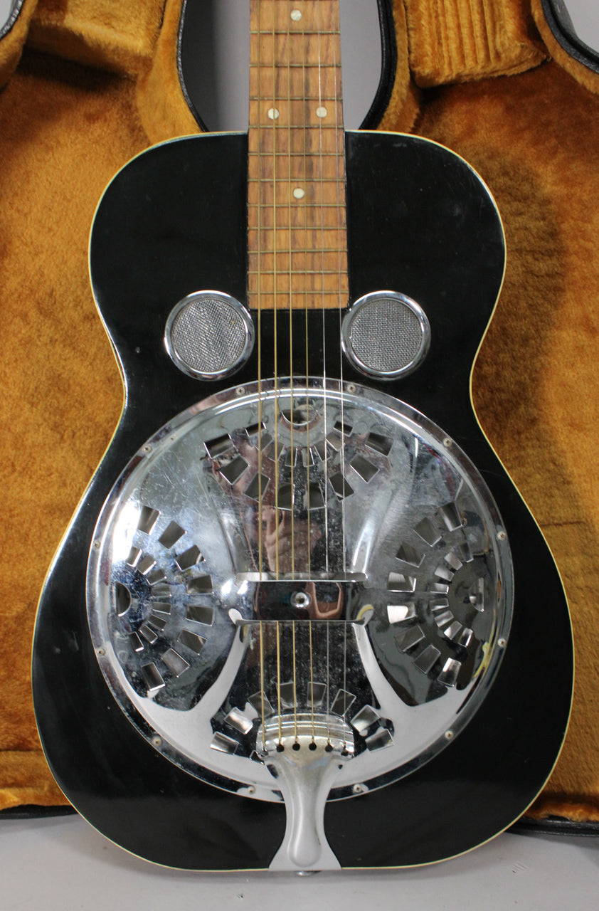 The black resonator guitar is centered, showing its shiny chrome cover plate with circular cutouts and two round sound screens.