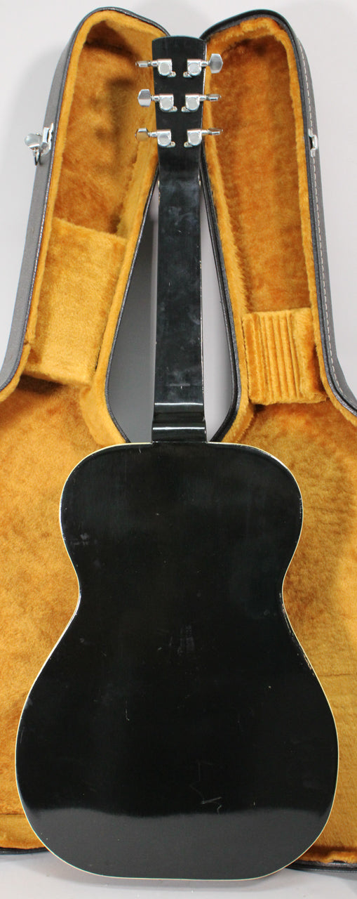 The black lap steel guitar is shown from the back, with its headstock and body resting in a plush orange-lined case.