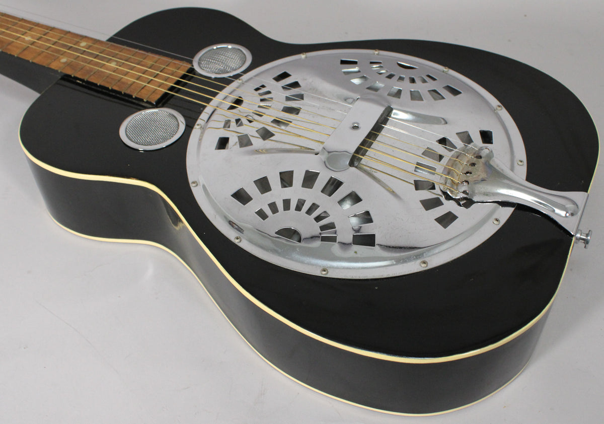 Close-up of the black resonator guitar's body, showing the chrome resonator plate with fan-shaped cutouts and two round sound holes.