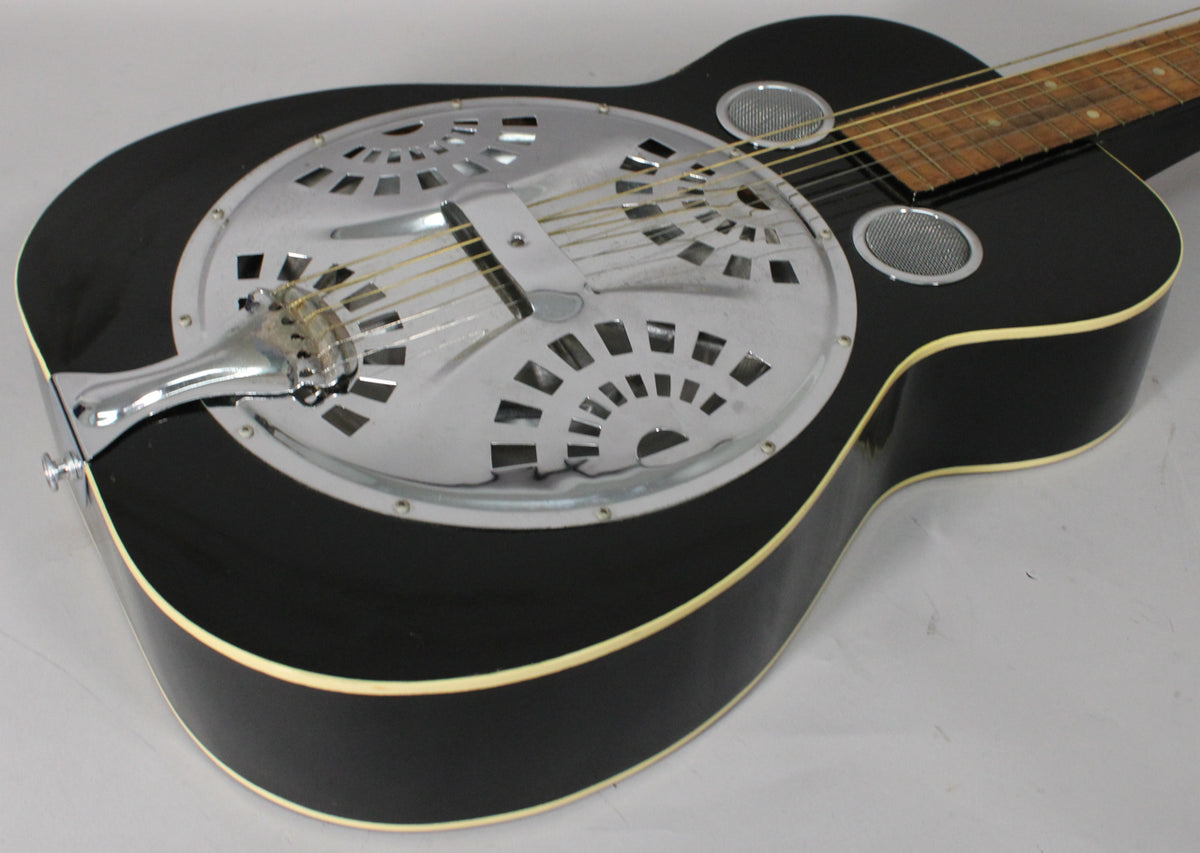 The black resonator guitar is angled from the lower bout, showing the chrome resonator cover with fan-shaped cutouts.