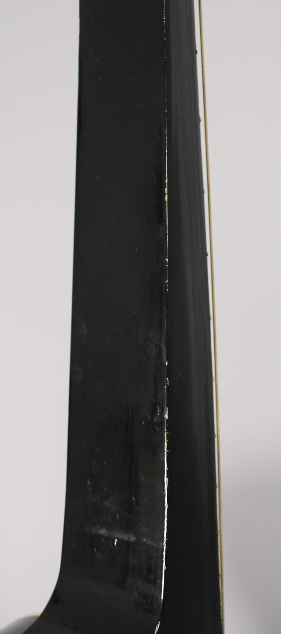 Close-up of the black square neck's edge, showing significant finish chipping and wear along the binding and some surface scratches.