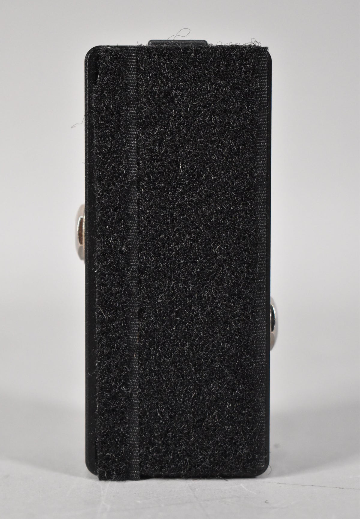 The black pedal is viewed from the side, showing its full height, with black hook-and-loop tape covering the bottom.