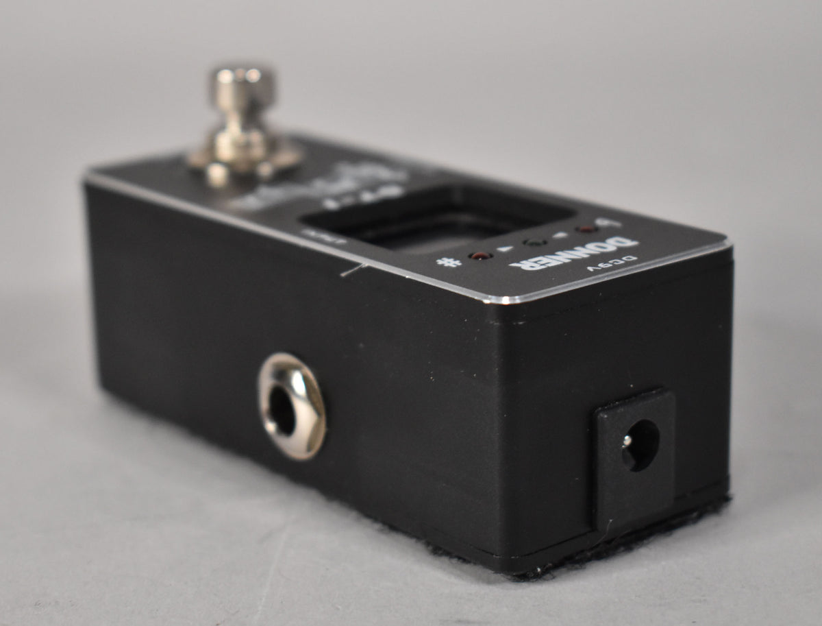 The black metal pedal is angled to show the input jack on the left and the power input on the right, with a silver footswitch.