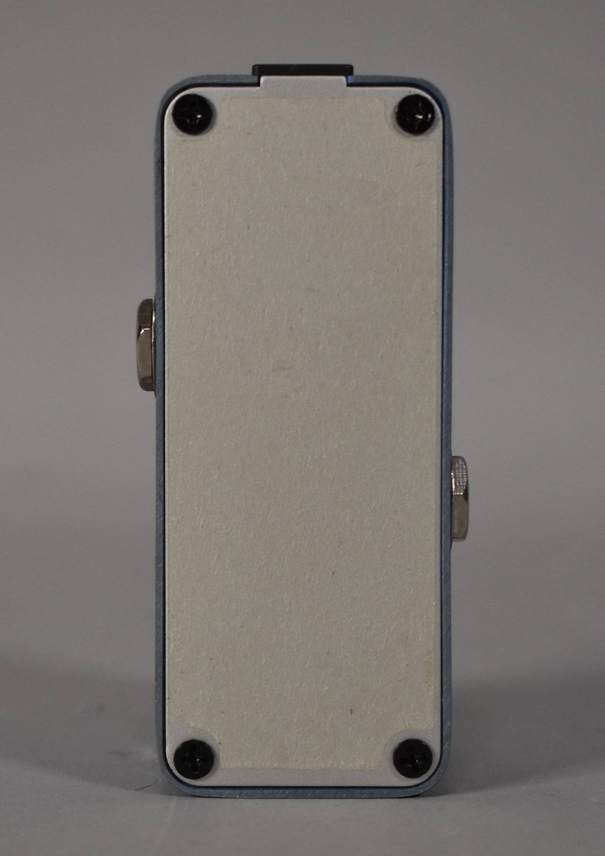 The pedal is viewed from the side, showing its light blue casing, a cream-colored base plate, and two silver nuts on the sides.