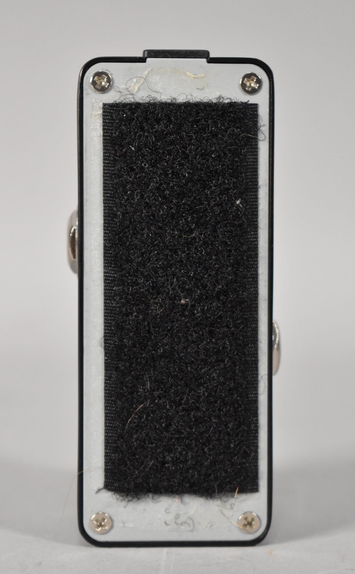 The pedal's underside is visible, showing a large strip of black hook-and-loop fastener and four silver screws on a white base.
