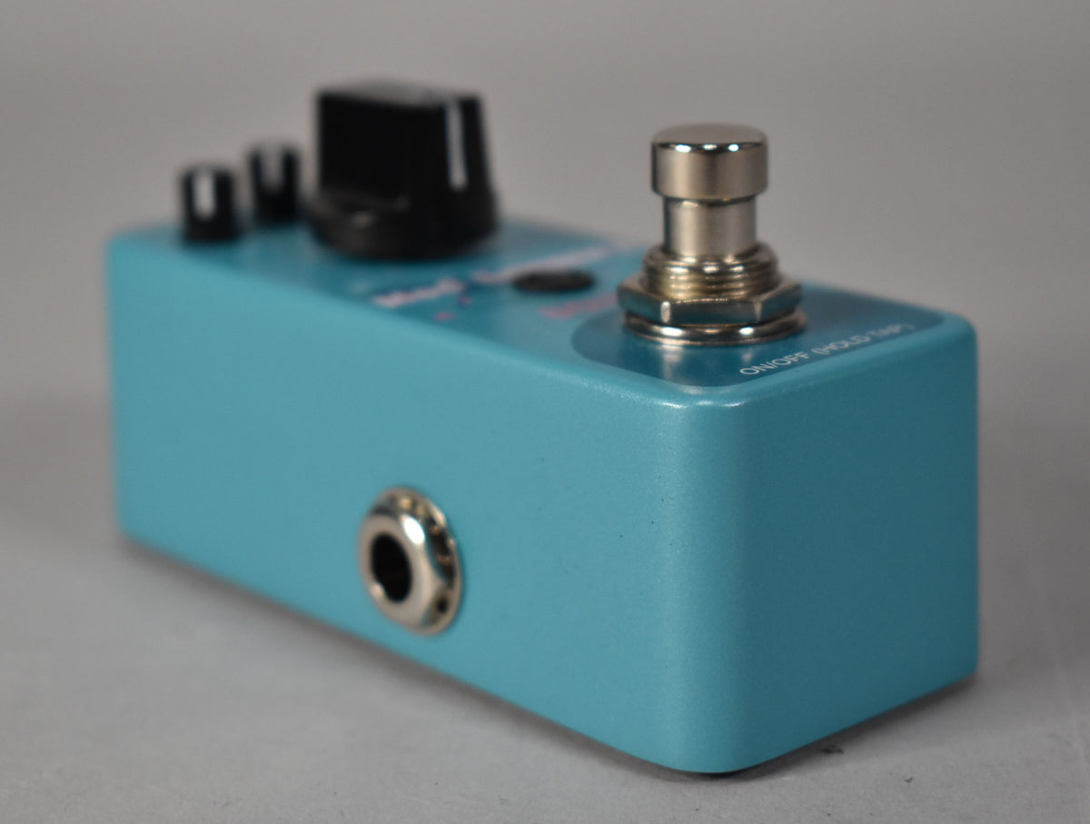 The turquoise pedal is angled from the right, showing a silver input jack, two black knobs, and a silver footswitch.