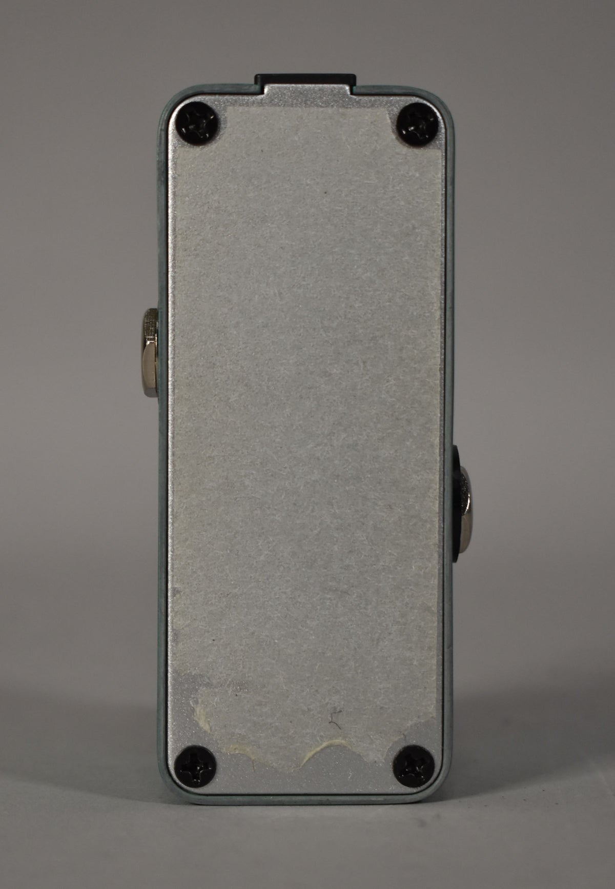 The reverb pedal is shown from the bottom, revealing a brushed silver backplate with four black screws and some adhesive residue.