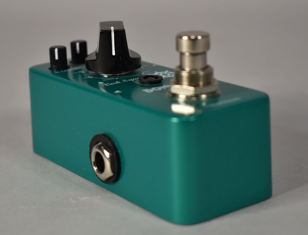 A teal reverb pedal, viewed from the front right, showing a large black knob, two smaller black knobs, a silver footswitch, and a silver input jack.