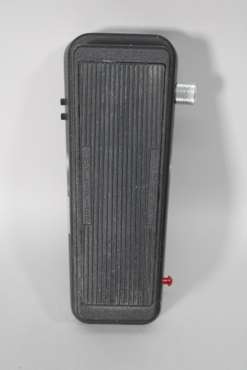 A black wah pedal, viewed from above, shows a ribbed footpad, a silver knurled knob on the right, and a red switch on the lower right.
