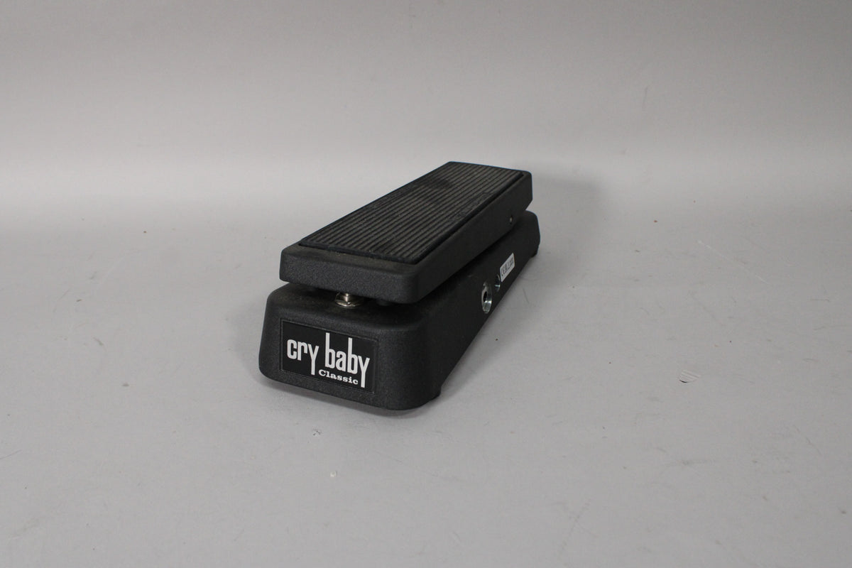 A black wah pedal with a textured finish, seen from a low angle, showing the ribbed foot treadle and two input jacks on the right.