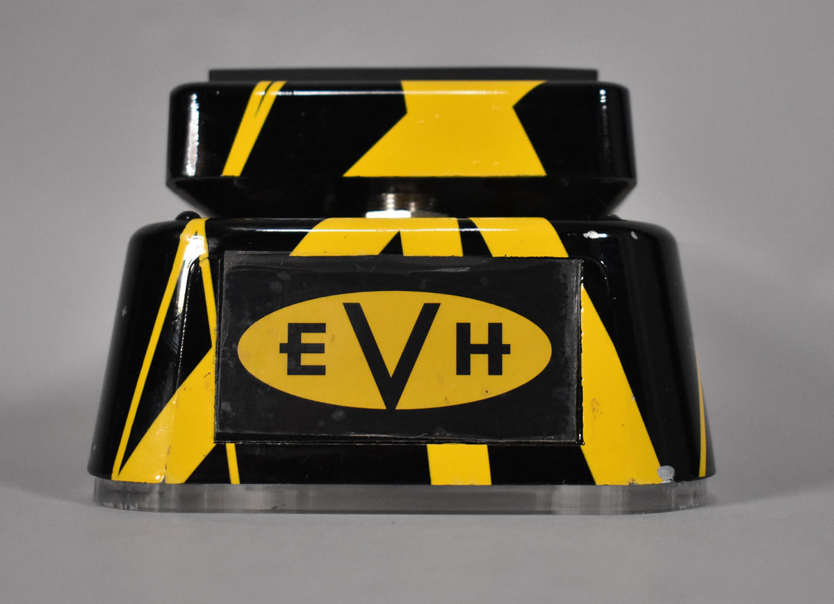 The black wah pedal, painted with yellow stripes, is viewed from the front, showing a central yellow oval with black lettering.