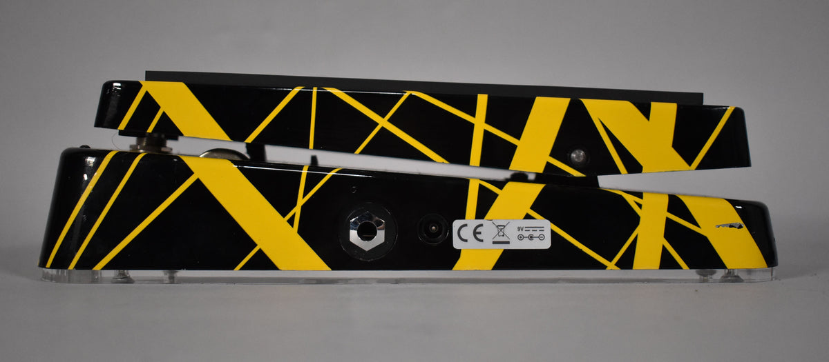 The wah pedal is seen from the right side, revealing its black finish with yellow stripes, input jack, and power port.