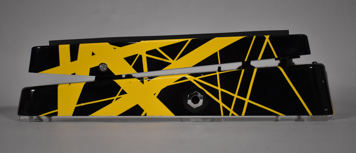 The black wah pedal, decorated with yellow stripes and geometric shapes, is seen from the side with a visible input jack.