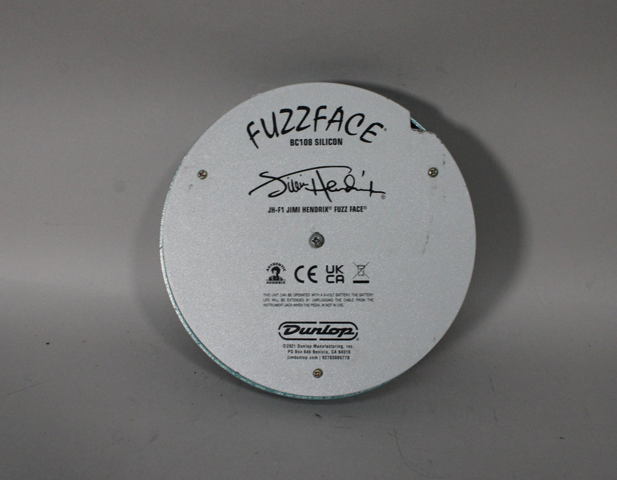 The circular pedal's light gray underside is visible, with black text and a signature, secured by four small screws.