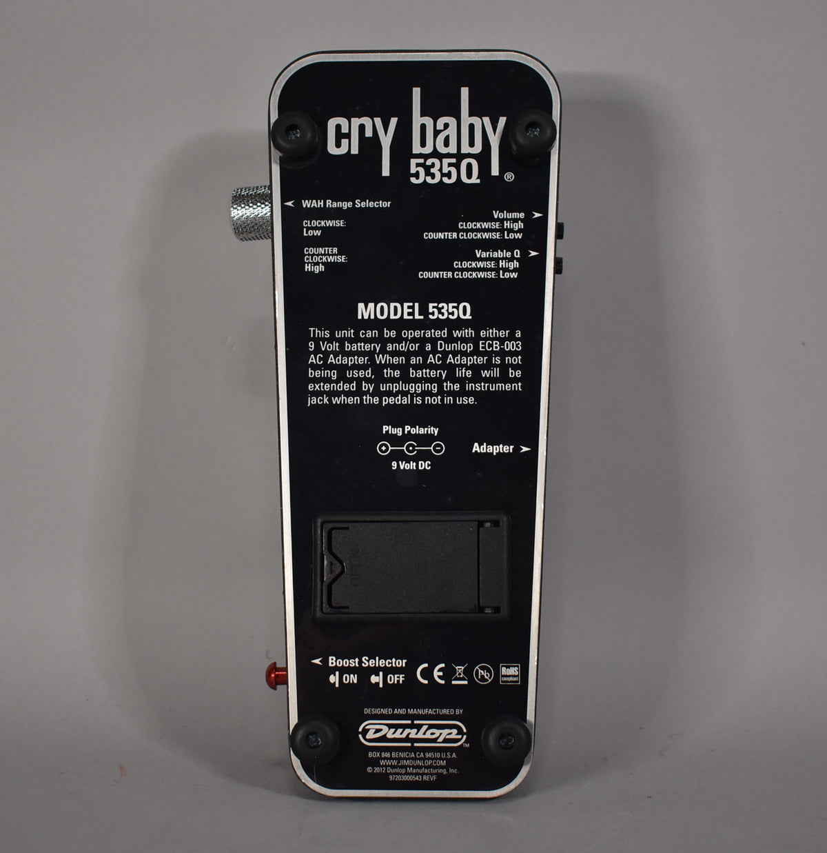 The black wah pedal's underside is shown, featuring a battery compartment, boost selector switch, and control labels.