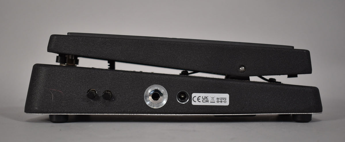 The black textured wah pedal is viewed from the right side, showing two small black knobs, a chrome input, and a power jack.