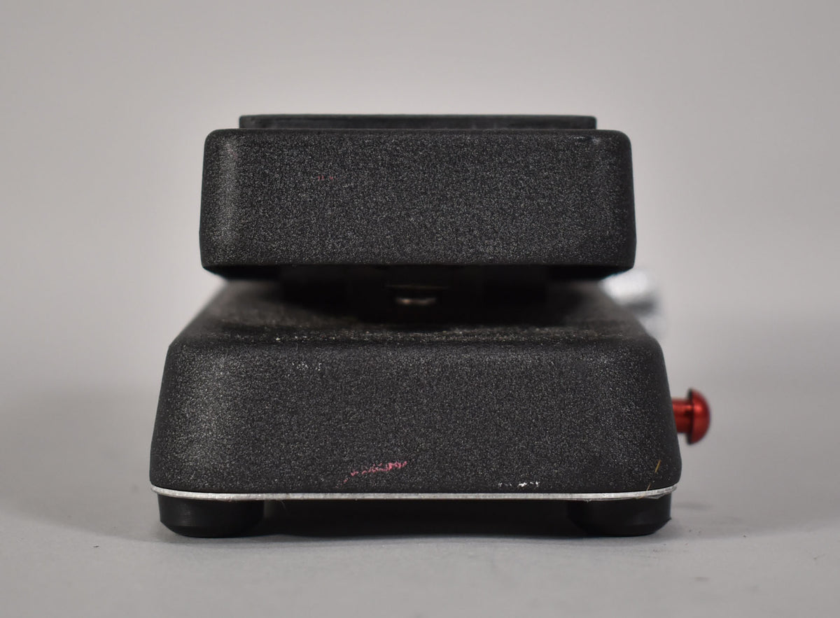 Side view of the black textured wah pedal, showing the raised foot pedal, silver trim, rubber feet, and a red knob on the right.