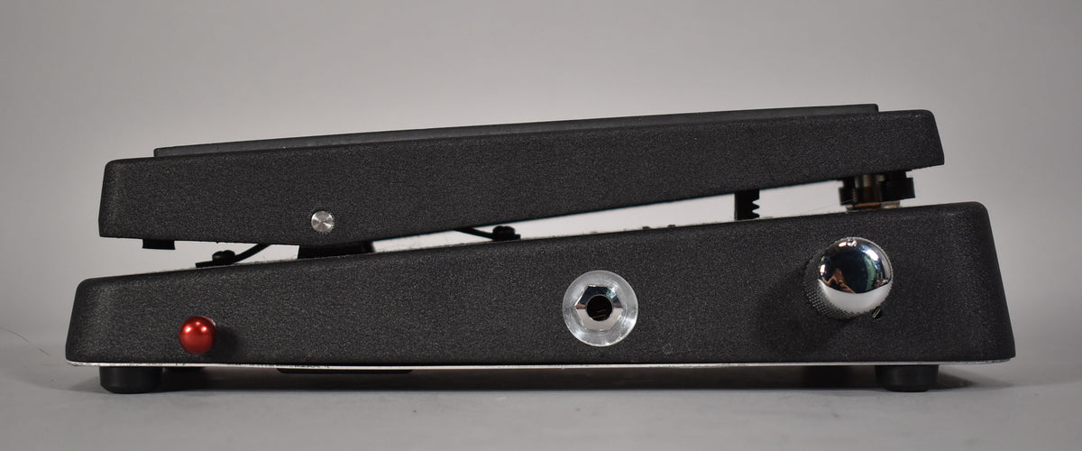 Side view of the black textured wah pedal, showing the red LED, input jack, and chrome knob on the right side.