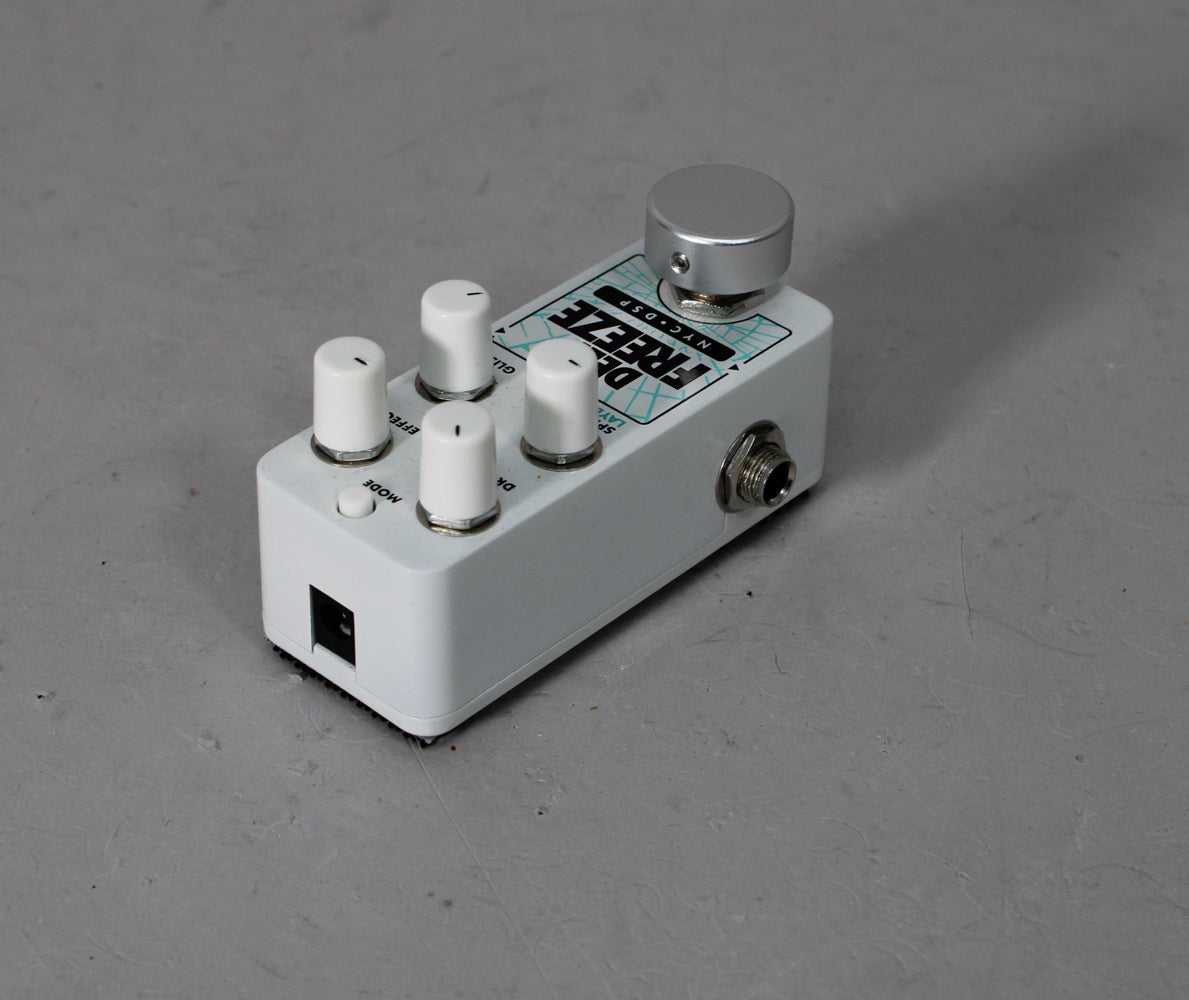 White guitar pedal with four small white knobs, one small white button, and one large silver knob, angled from the right.