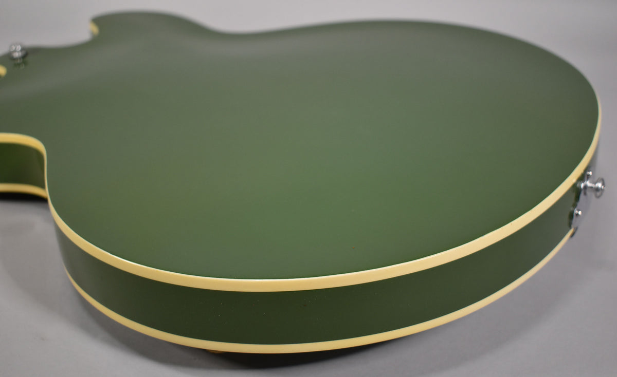 Close-up of the guitar's olive drab body and side binding, showing a matte finish and a strap button on the lower bout.