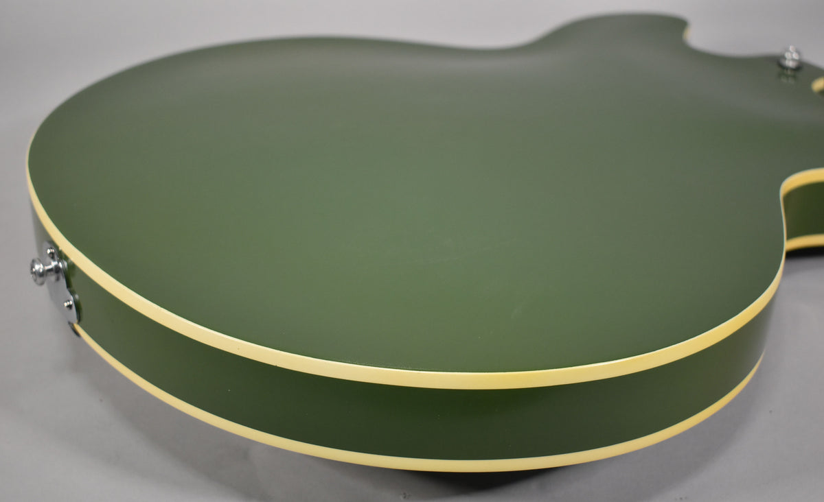 Close-up of the olive drab hollowbody's lower bout, showing the matte finish, cream binding, and a chrome strap button.