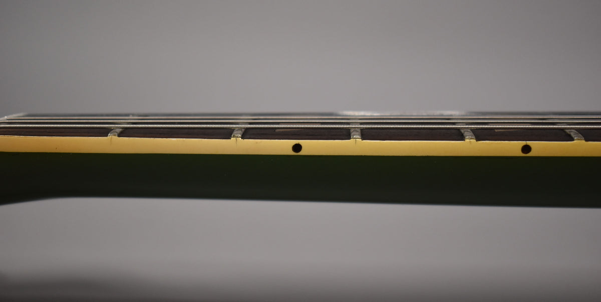 Side view of the guitar neck, showing the dark fretboard, worn frets, and cream binding with small dark dot markers.