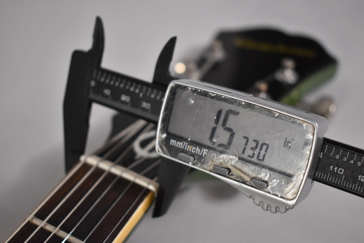 A digital caliper measures the guitar's nut width at 1.5730 inches, with the fretboard and headstock visible.