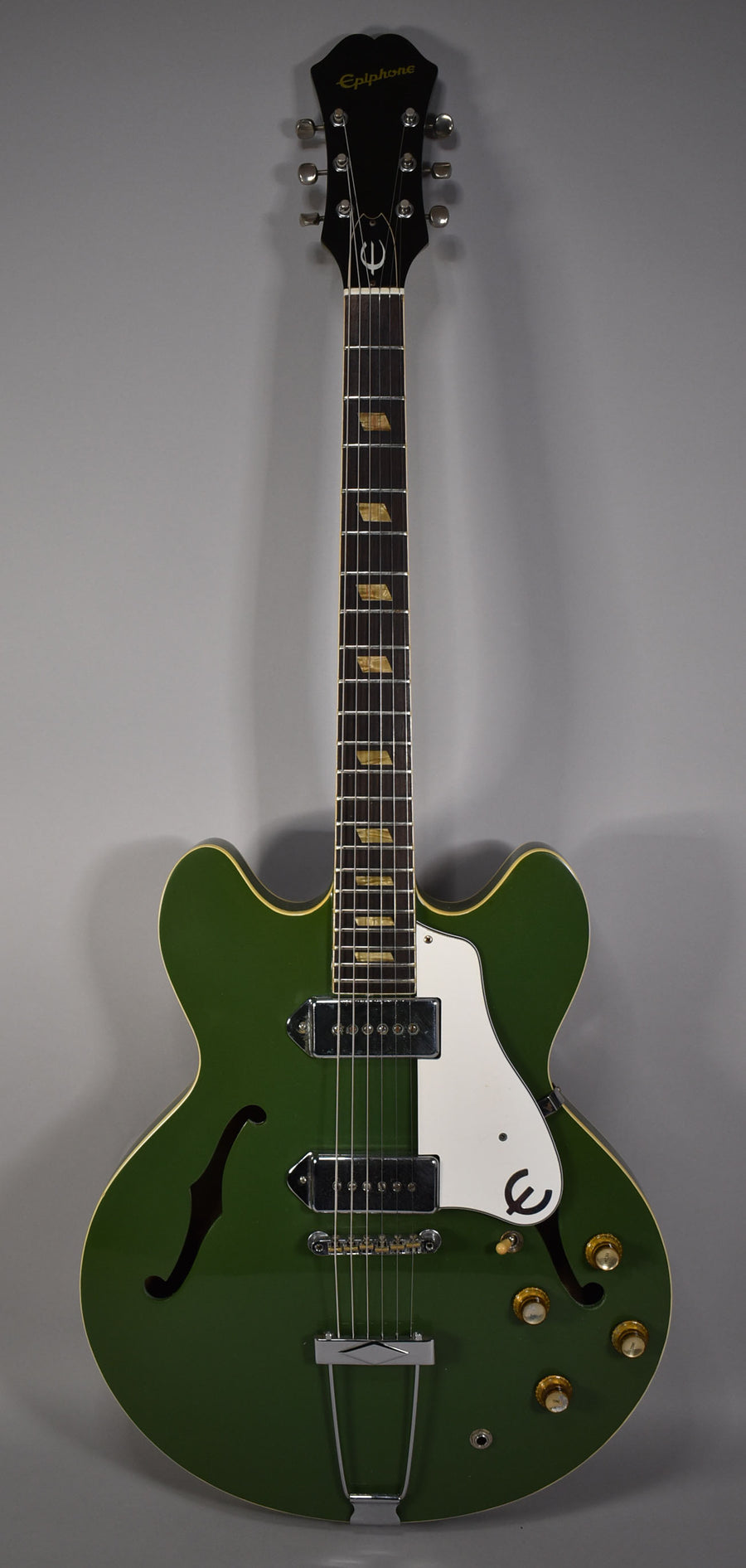 Full-length view of a glossy olive drab hollowbody electric guitar with a white pickguard, two P90 pickups, and four gold knobs.