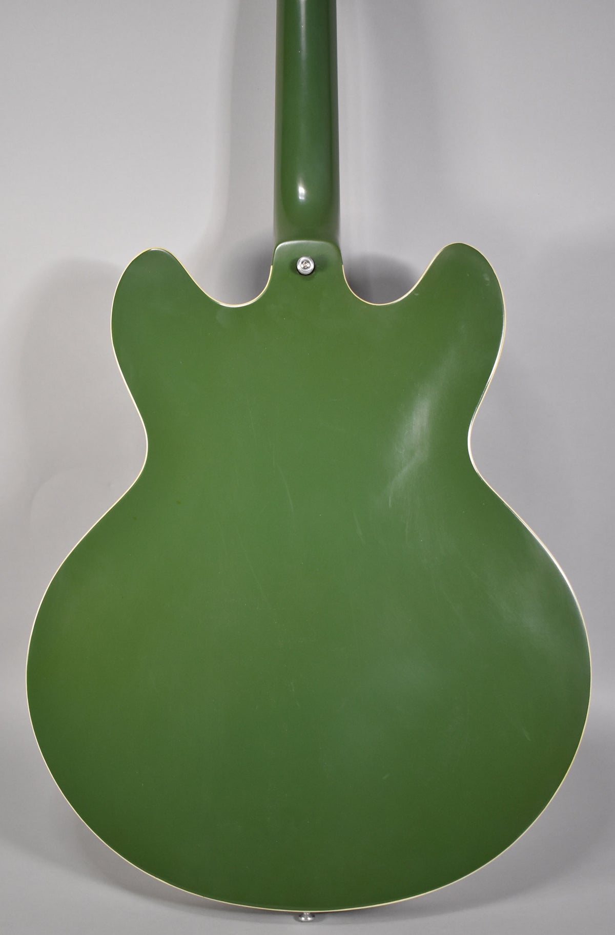 The back of an olive drab hollowbody guitar with a glossy finish, showing light scratches and a strap button.