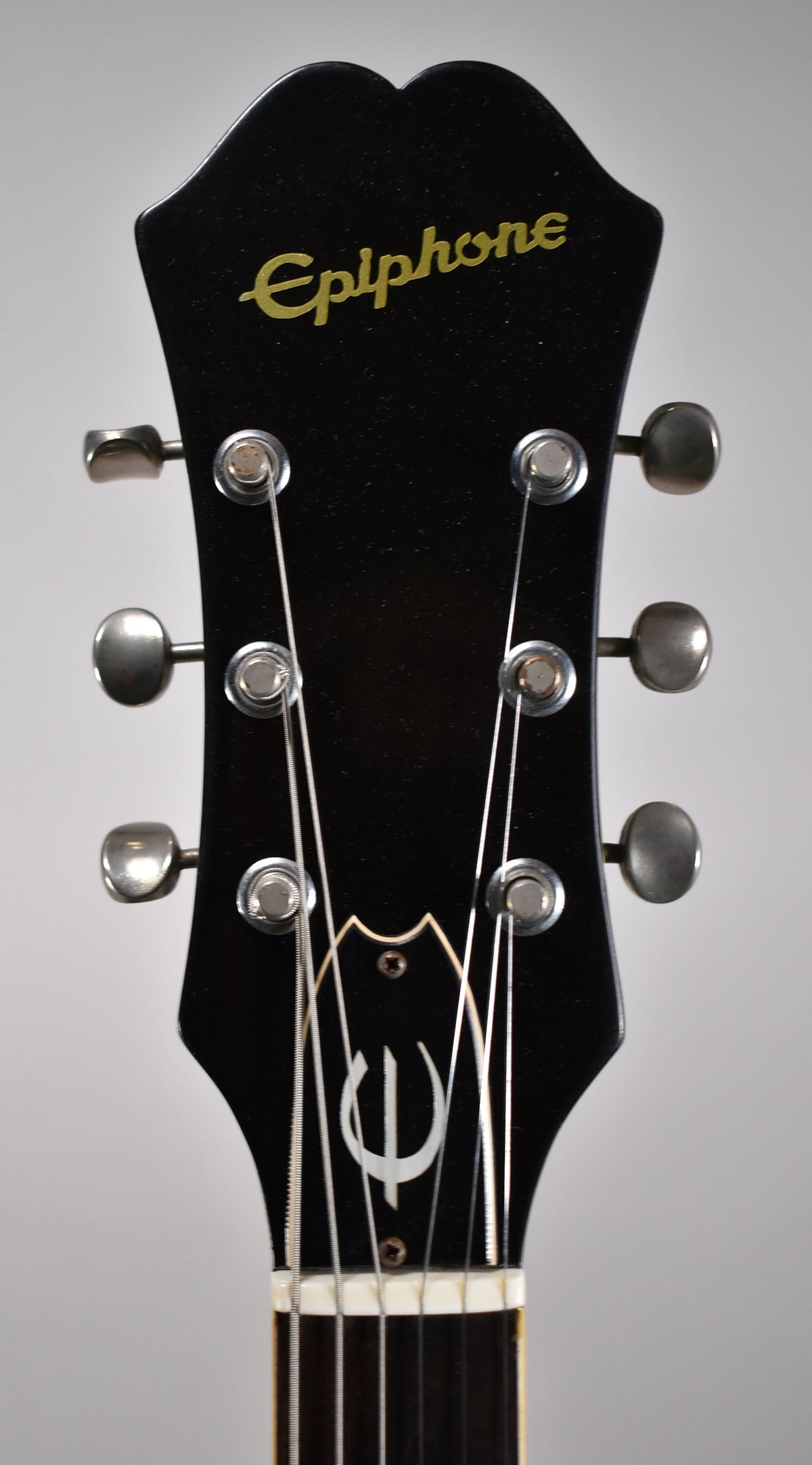 Close-up of the black headstock with gold script logo, six metal tuners, and a white inlaid symbol.