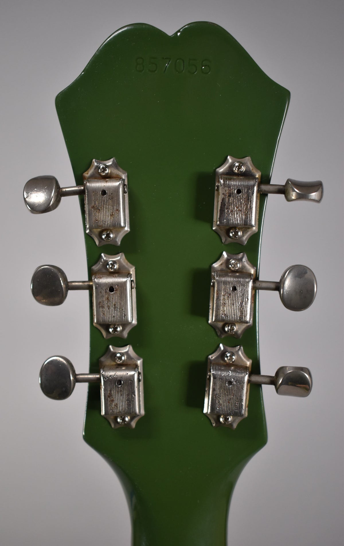 The back of a dark green guitar headstock with six tarnished, rectangular tuning machines and oval buttons.