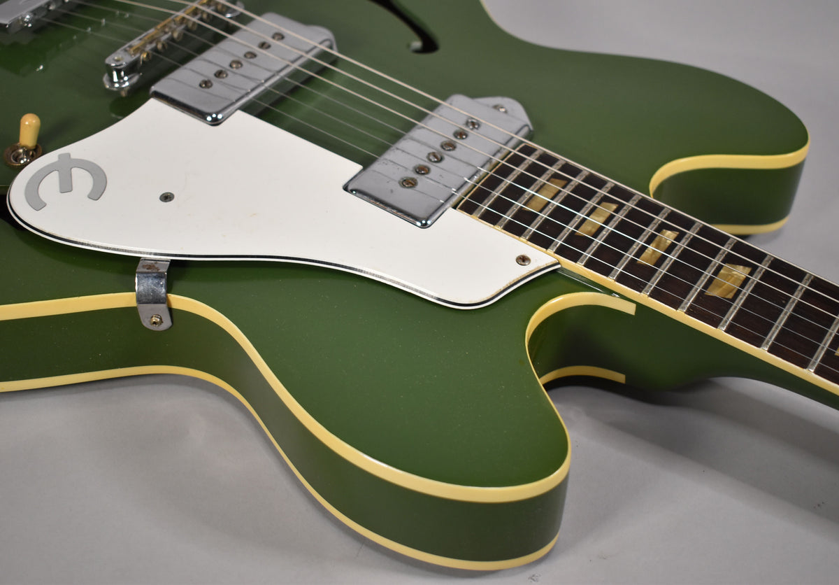 Close-up of the olive drab body and neck, showing the white pickguard, chrome pickups, and trapezoid fretboard inlays.