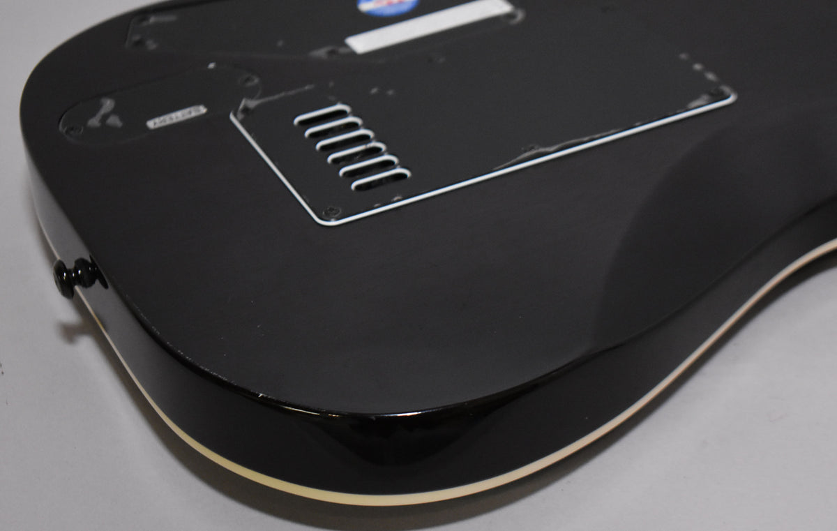 The guitar's charcoal burst back shows a matte finish, glossy binding, and a battery compartment near a vented control cavity.