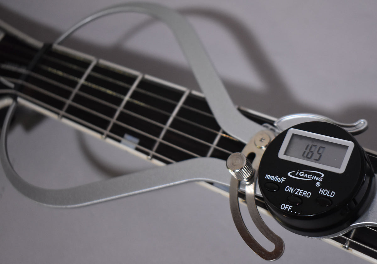A digital caliper measures the guitar's nut width at 1.69 inches, resting on the fretboard with block inlays.