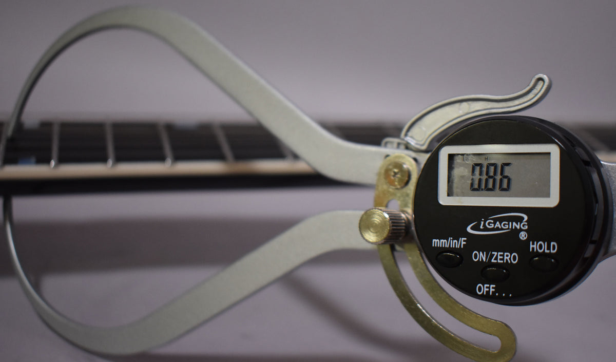 A digital caliper measures the guitar's fret height at 0.86, showing the dark fretboard and light frets from a side angle.