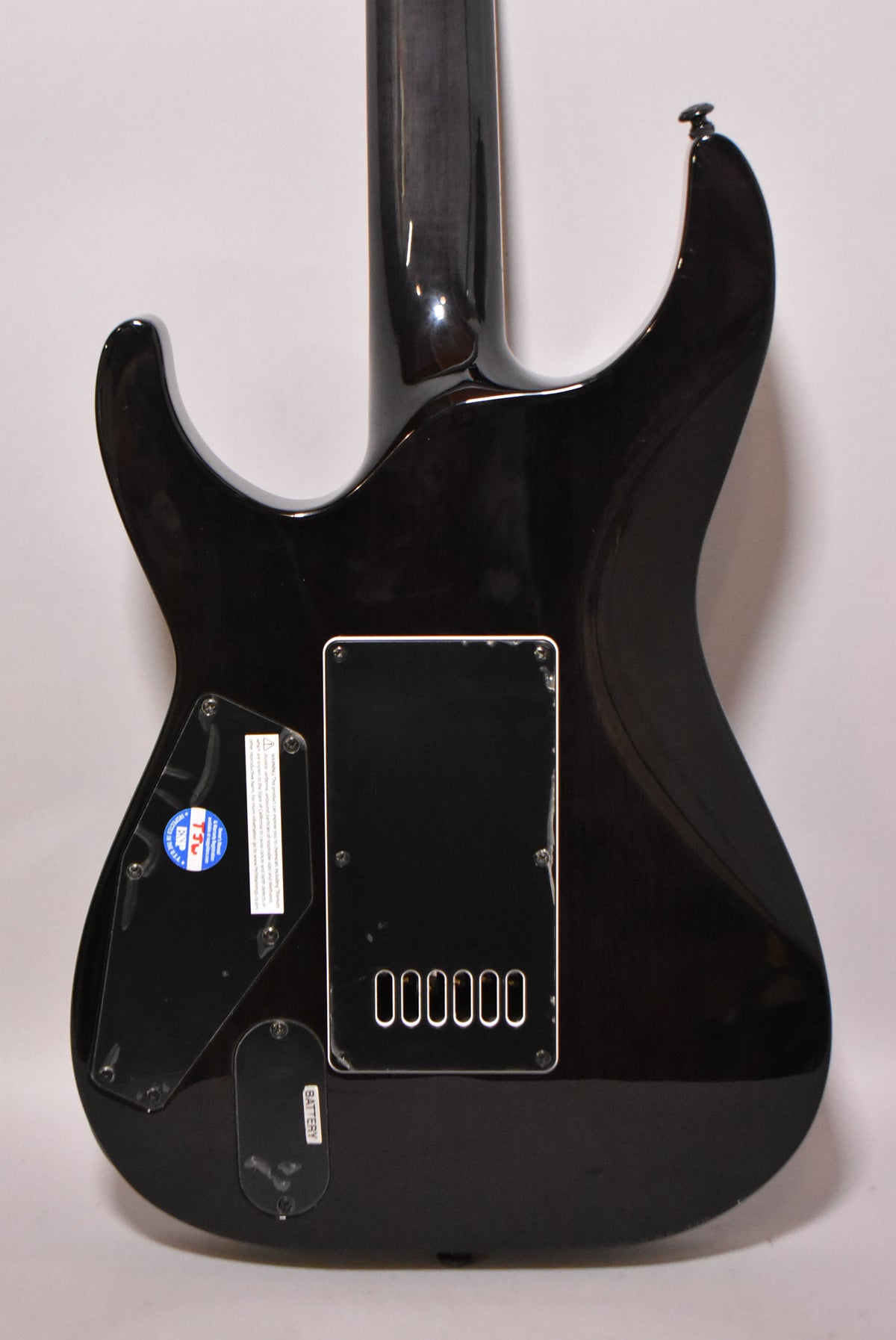 The back of a dark charcoal burst electric guitar, showing the neck joint, control cavity, and battery compartment.