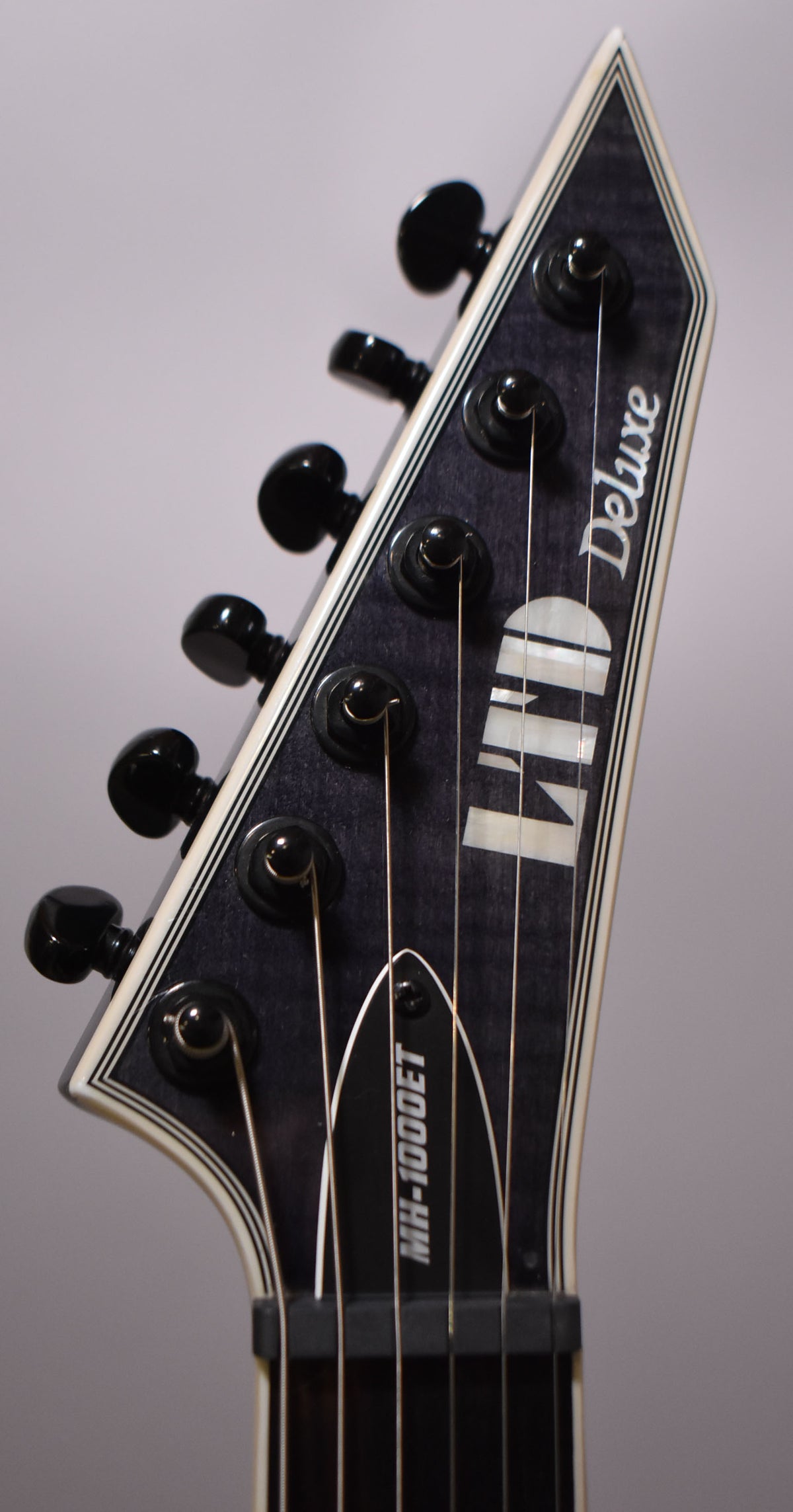 Close-up of the guitar's pointed headstock, angled left, showing six black tuners on a charcoal burst finish with white binding.