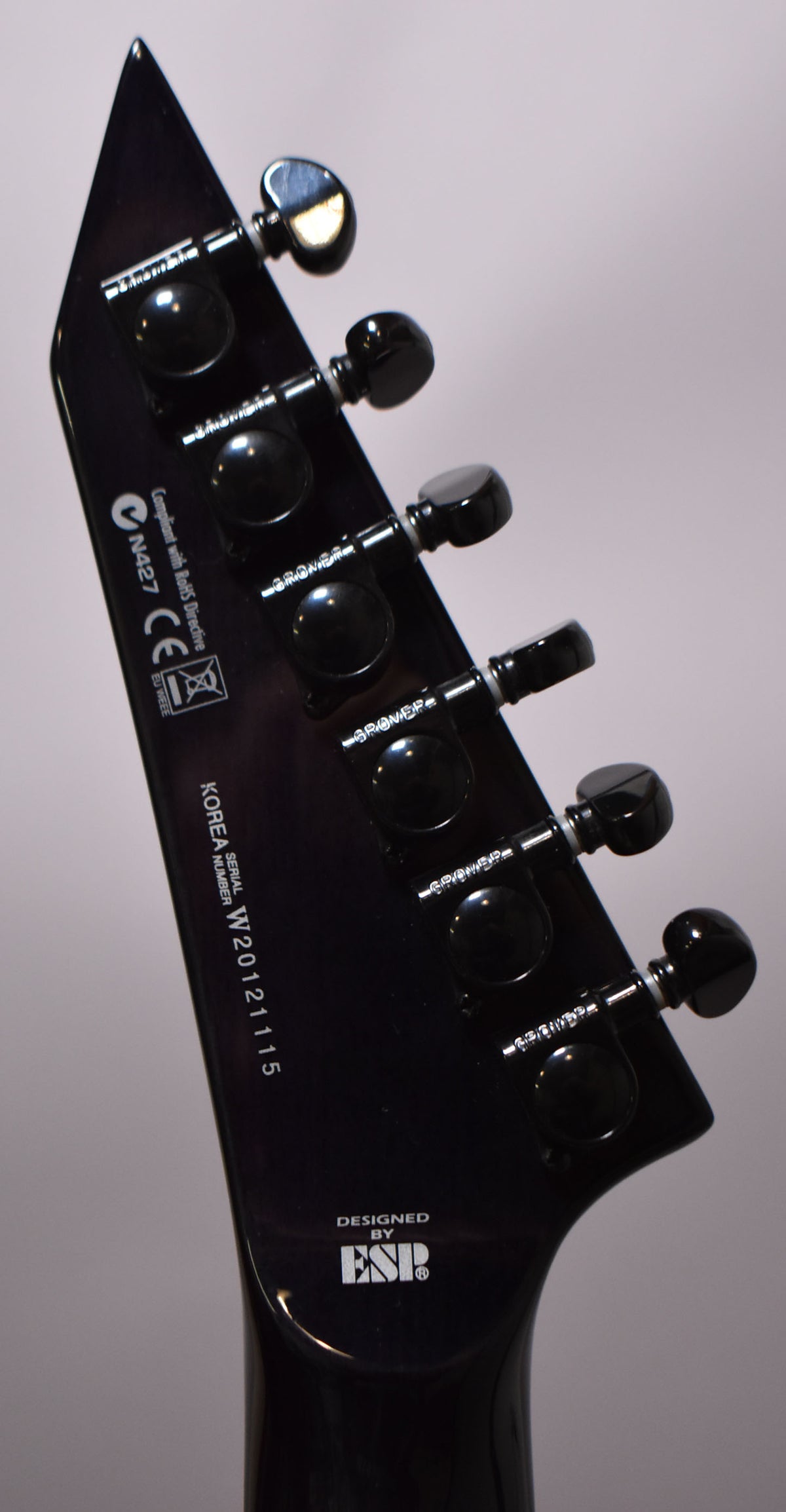 The guitar's dark purple headstock, angled left, shows six black Grover tuners and a glossy finish with minor reflections.