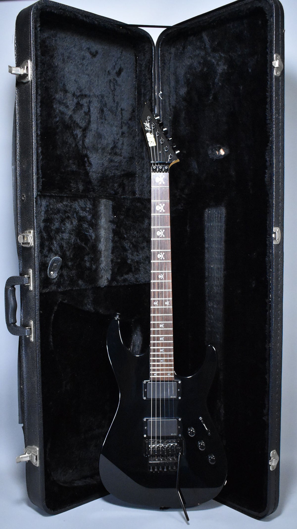 Full-length view of a glossy black electric guitar with skull and crossbones fret inlays, resting in its open, black-lined hard case.