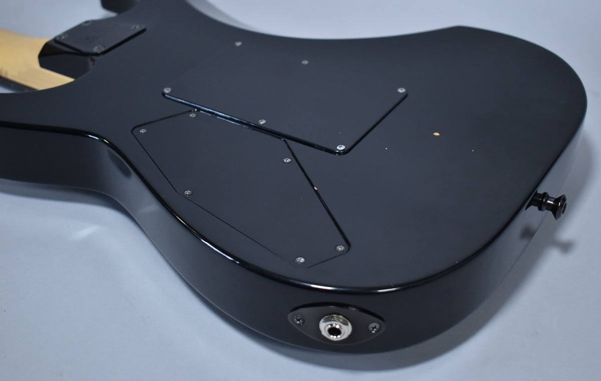 The guitar's glossy black back shows two control cavity covers, a strap button, and an output jack, with some minor wear.