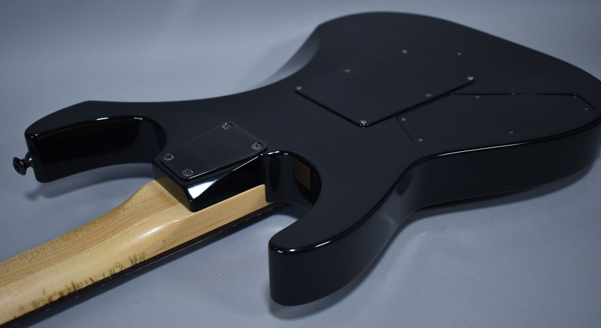 The guitar's glossy black body is seen from the back, with a light-colored neck and some wear visible near the neck joint.