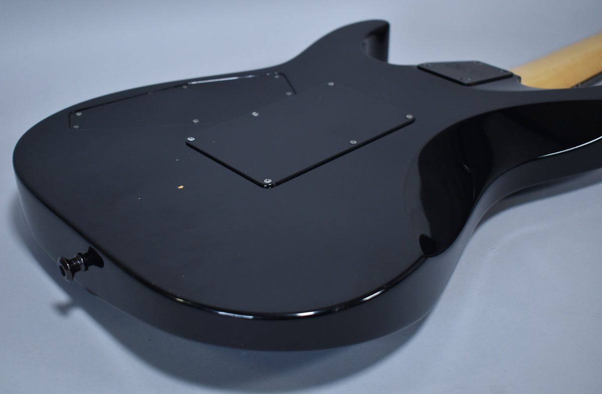 The guitar's glossy black back is angled, showing the output jack, two control cavity covers, and a few small dings on the lower bout.