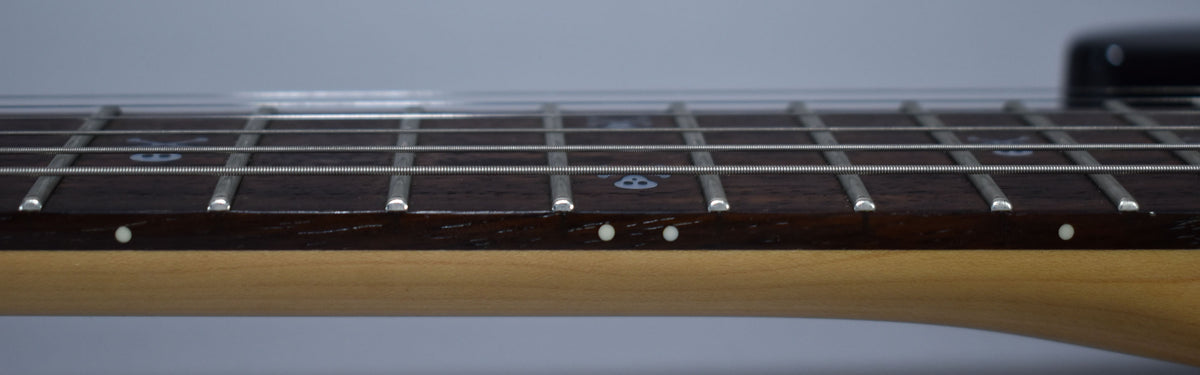 Close-up of the dark fretboard and light maple neck, showing white skull-and-crossbones inlays and side dots, with minor wear.
