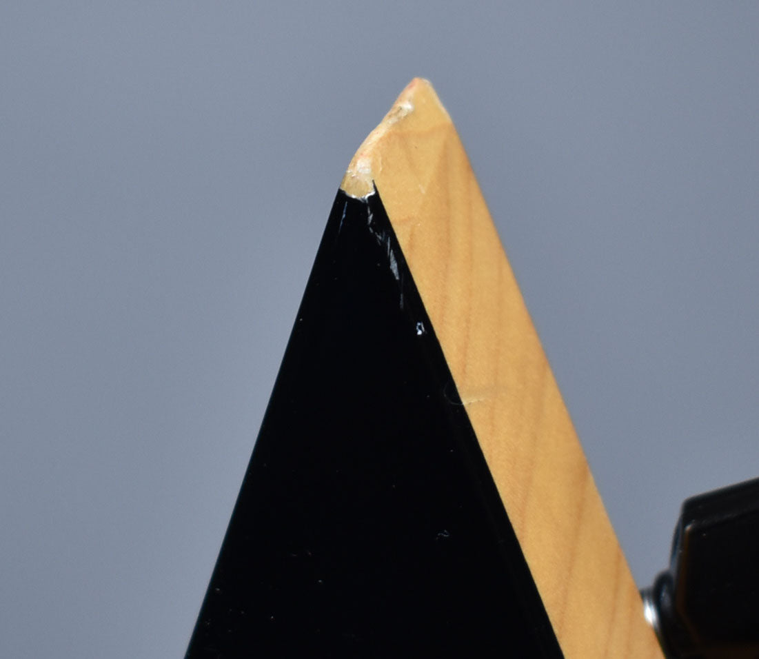 Close-up of the guitar's pointy headstock tip, showing a chip in the black finish revealing the light wood underneath.