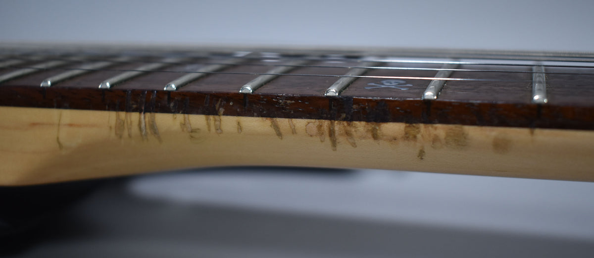 Close-up of the guitar's neck, showing heavy wear and dark discoloration on the light wood and dark fretboard, with a skull inlay visible.